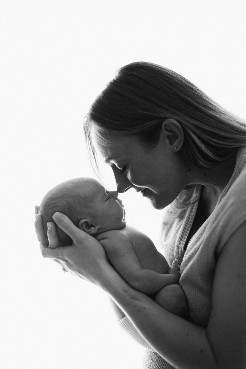 Mum holding newborn baby in her arms and touching noses at Billingshurst newborn photoshoot