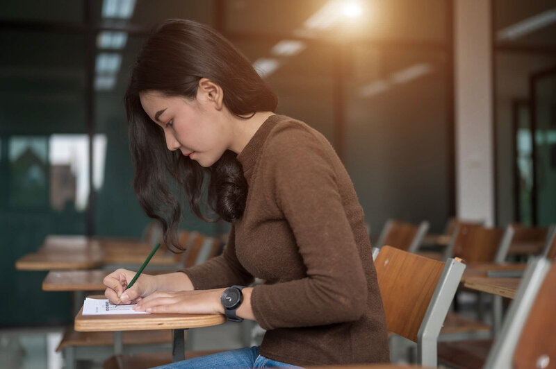 Female Asian PA student taking handwritten notes during a live exam prep coaching session