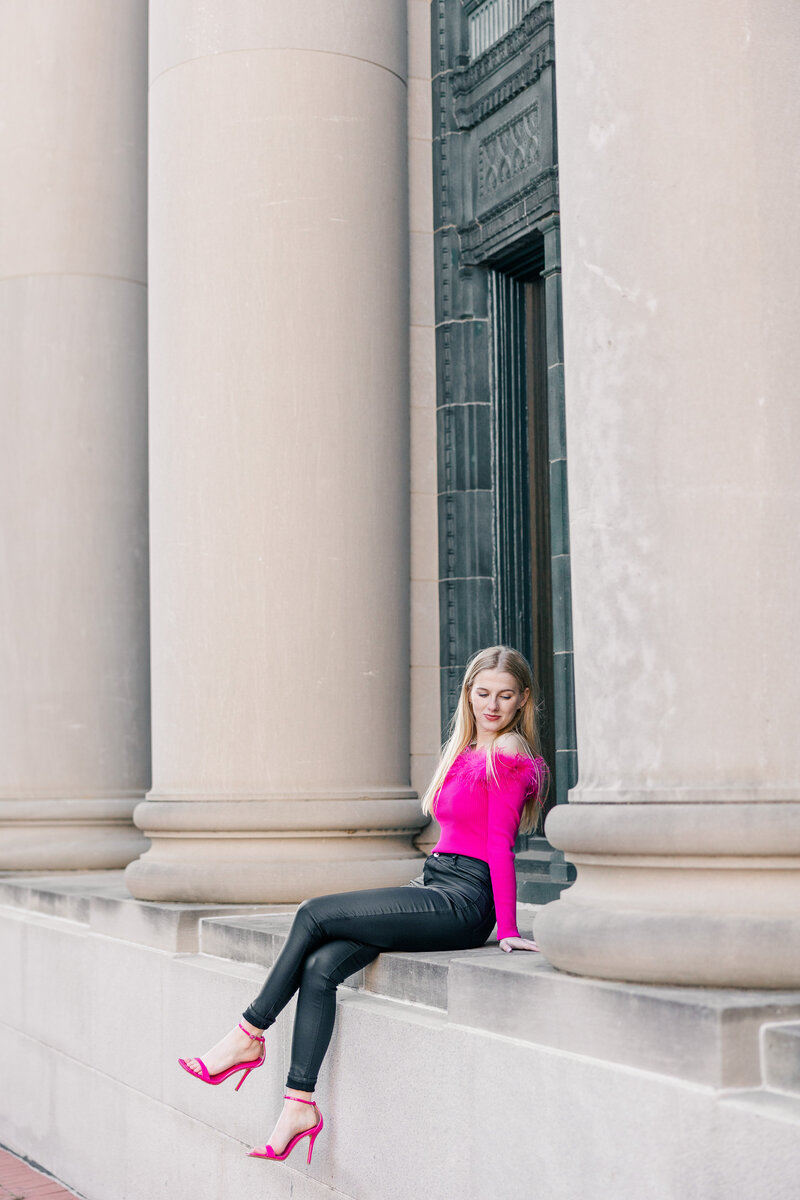 girl wearing hot pink sitting in between grand columns