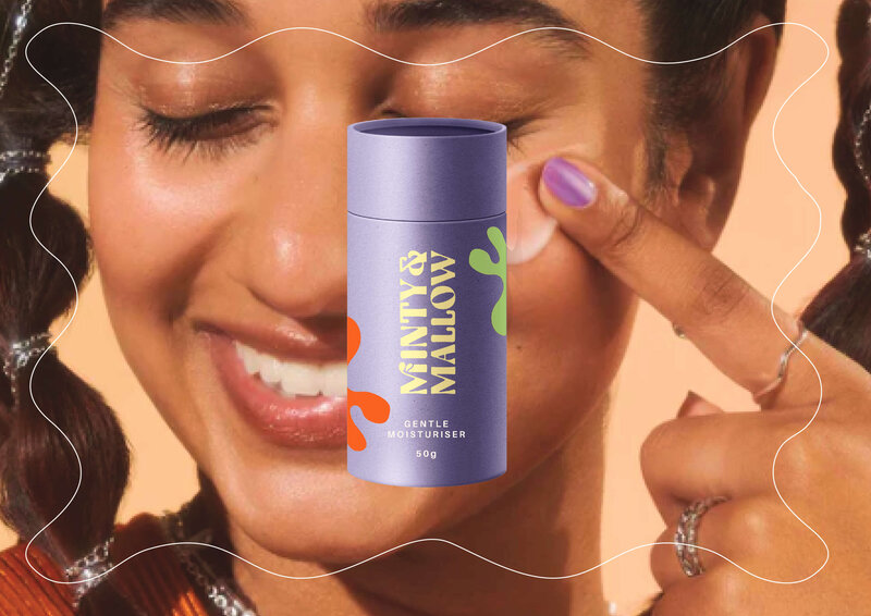 A close-up of a smiling woman applying a product from Minty & Mallow. The lavender-colored packaging features bold typography and playful abstract elements, reflecting the brand’s fun and vibrant personality.