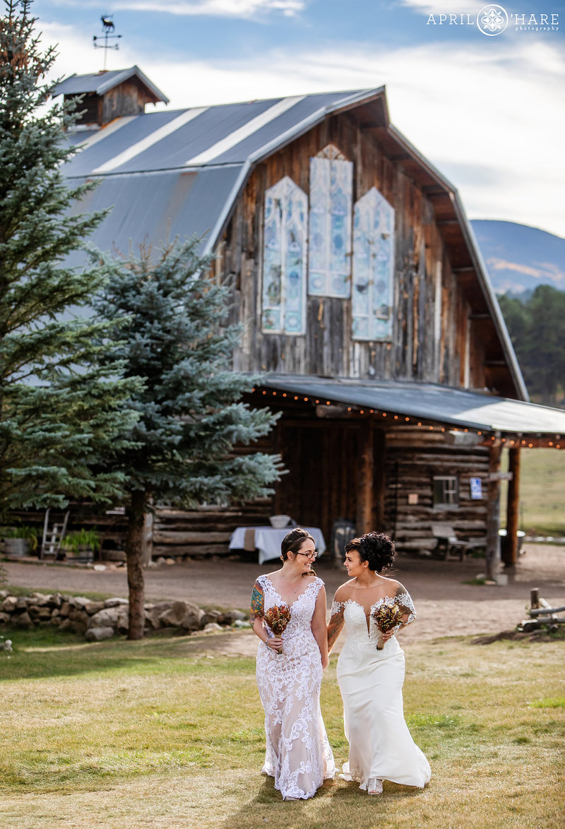 Two brides walk into their wedding ceremony holding hands at Barn at Evergreen Memorial Park
