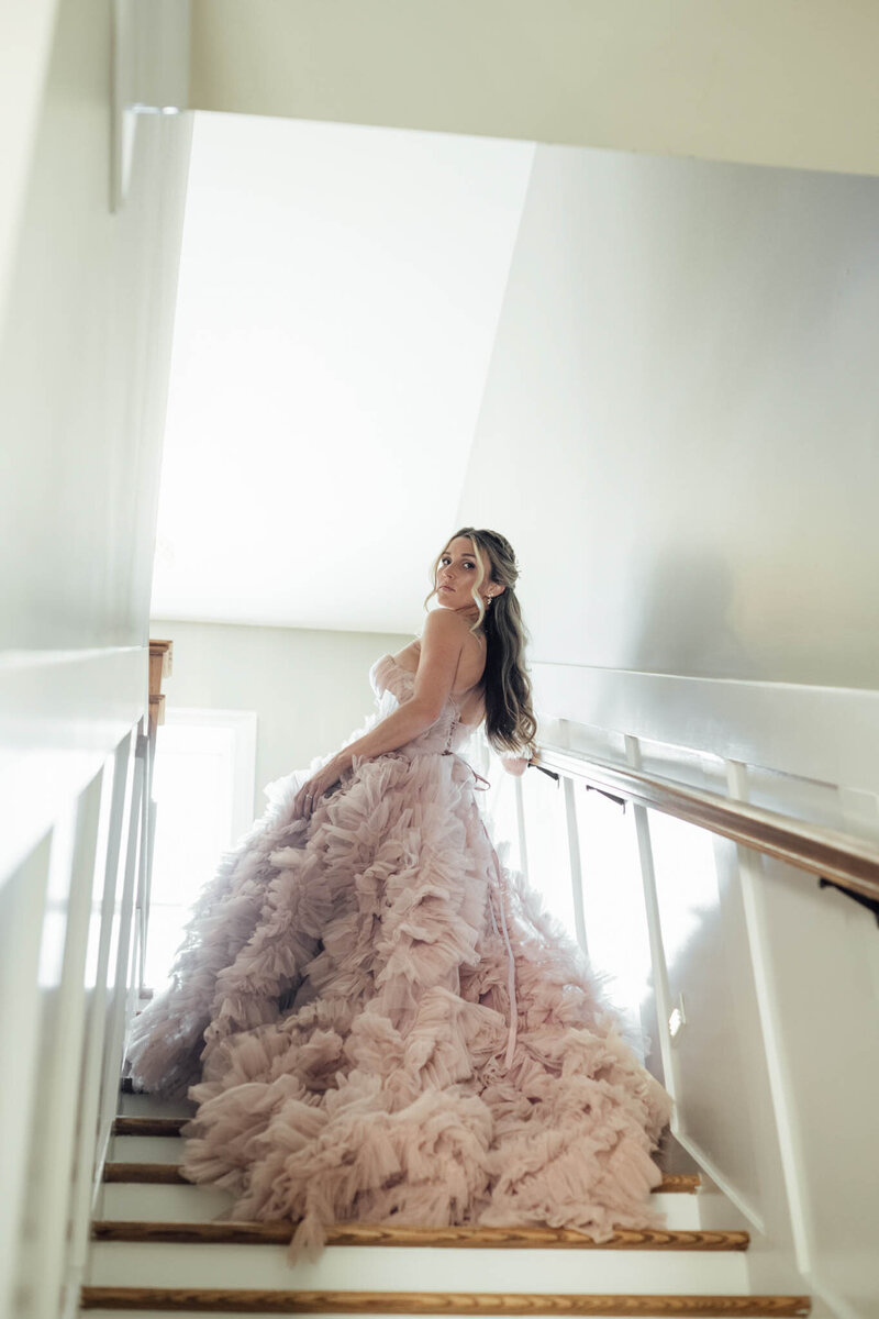 Bride in a pink ruffled gown posing on a staircase