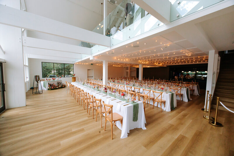 Elegant wedding reception setup with long banquet tables, wooden cross-back chairs, and string lights at The Gem venue in Canmore