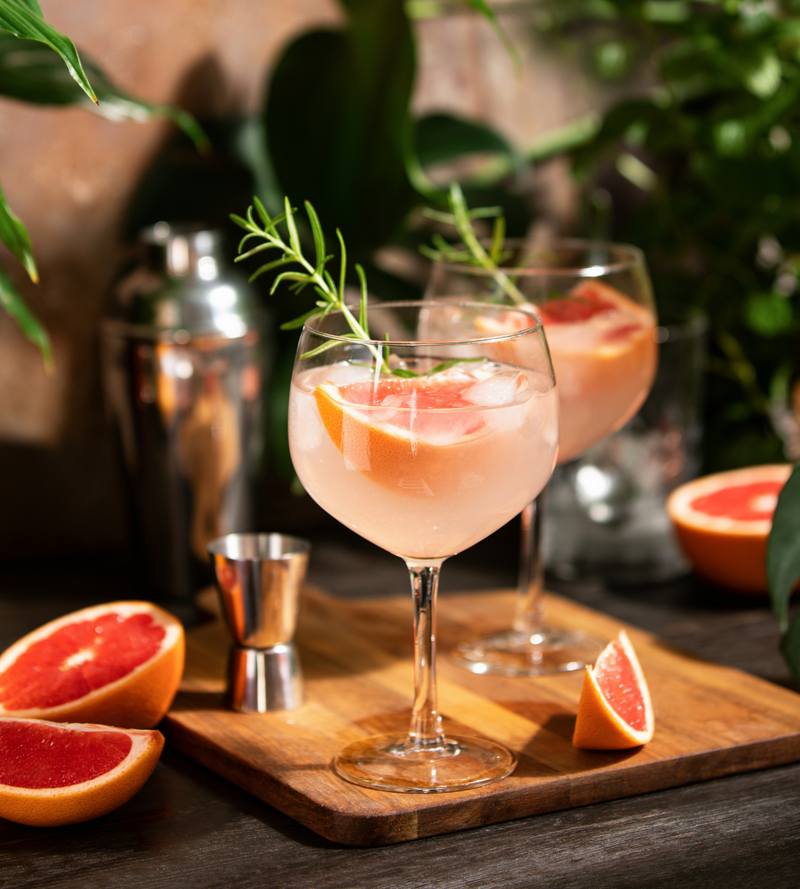 Grapefruit cocktail in a glass on a counter with pieces of grapefruit around it