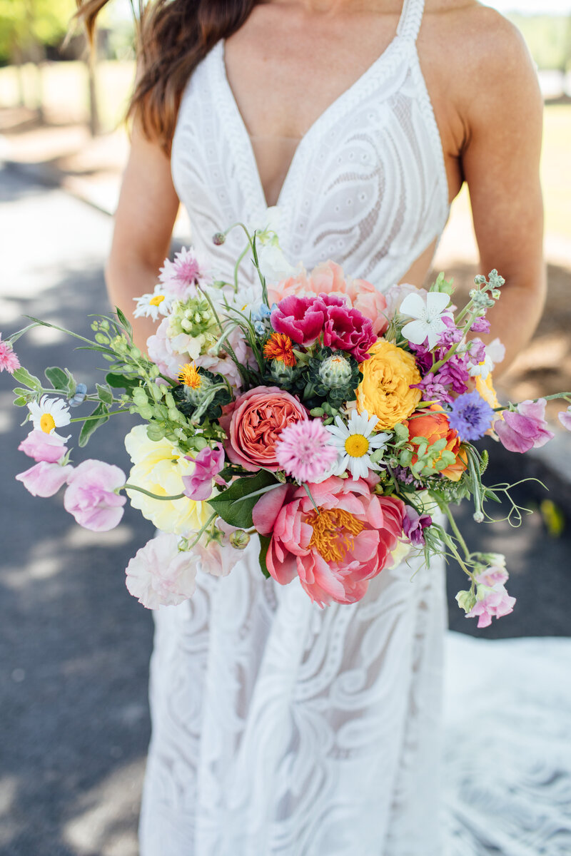 Girl in white dress holding a bouquet of pink, yellow, orange, white, and purple flowers 