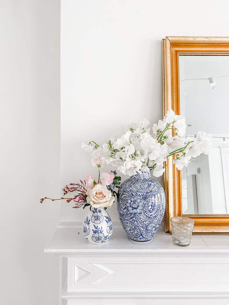 Two Blue & White Vases Filled with White Flowers on a Mantle - Brenda Chadambura