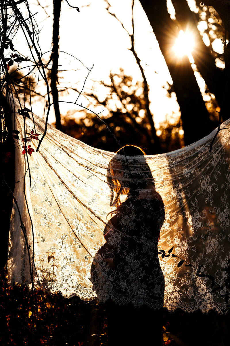 A silhouette of an expecting mother behind a sheet at sunset.  