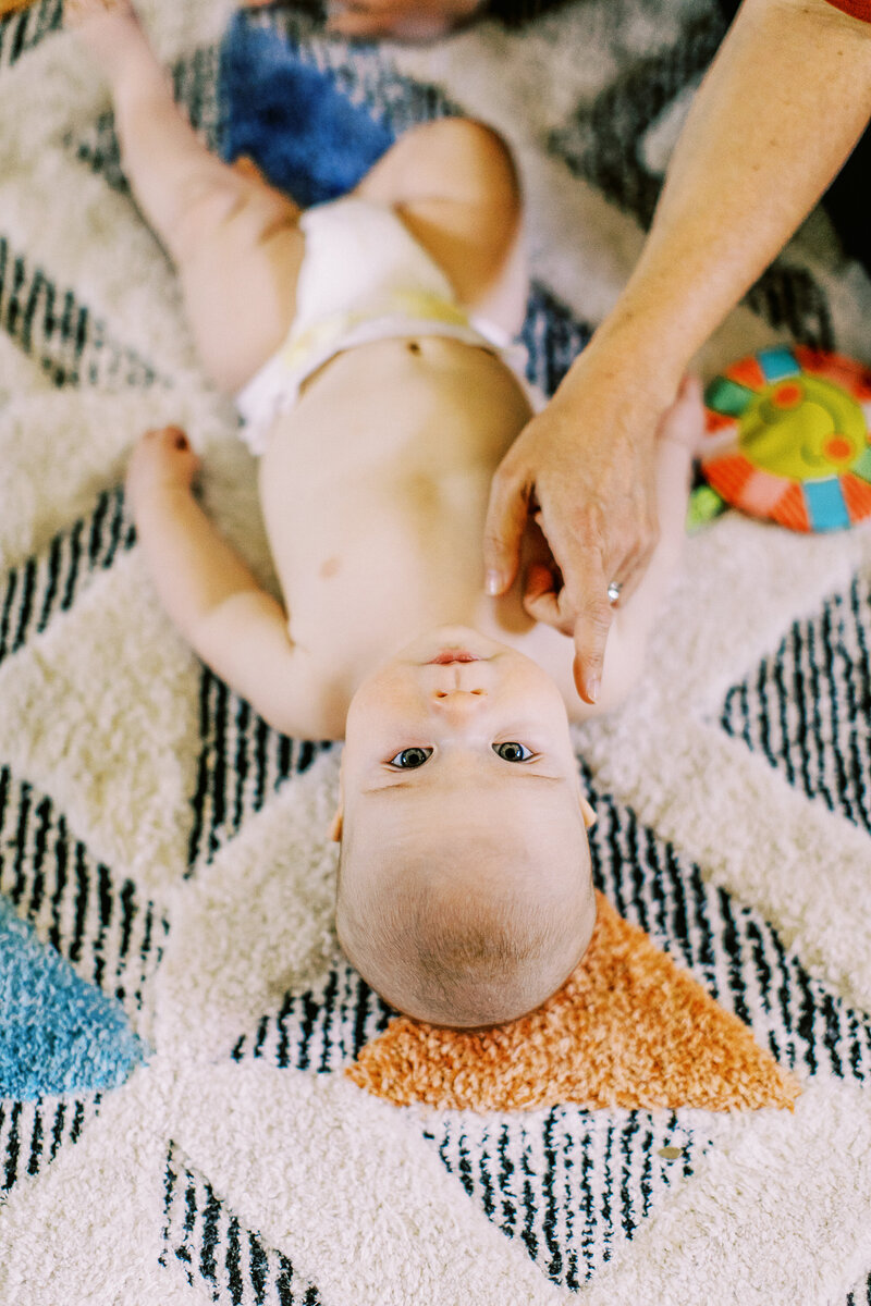 cute baby boy lies on a rug and looks back up to camera