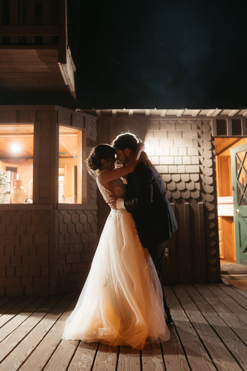Elopement Reception Ideas | Eloping couple sharing their first dance on a Chalet's porch with dramatic backlighting 