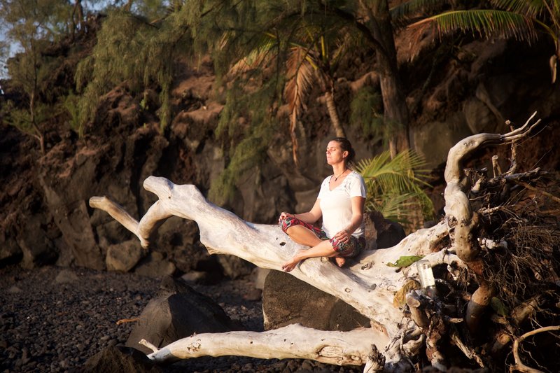 Yogini sitting on a log on the beach in Hawaii in meditation