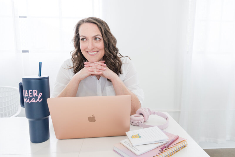 course creator and social media strategist working on her white desk. she is sitting on a green chair. on the desk there is an agenda, with a coffee mug and a green and pink flower