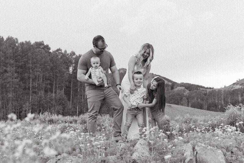 Family of five laughing together in a field of wild flowers.