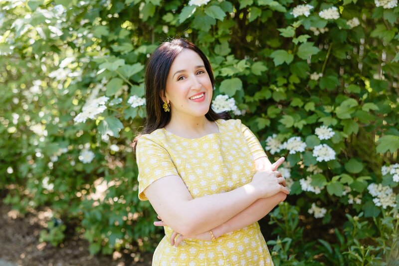 Woman with brunette hair wearing yellow dress against garden background
