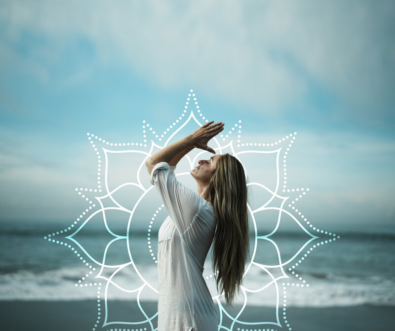 Noelle Rivet on a beach with hands in prayer with a beautiful chakra and ocean in the background