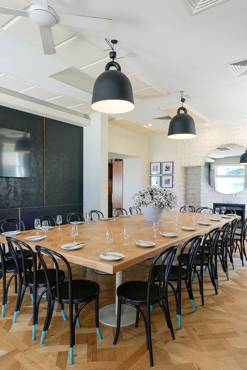 A restaurant with a large wooden tablea nd black chairs set up for dining