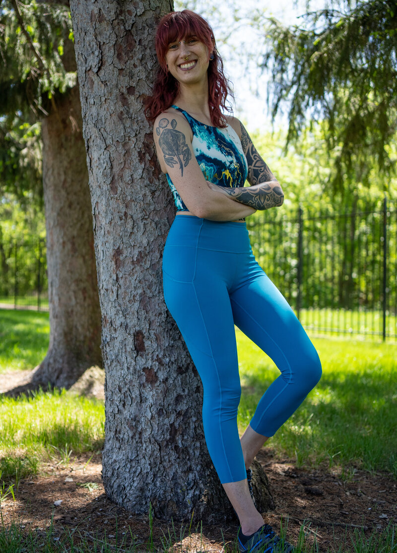 a woman in blue workout clothes leans against a tree to welcome strength training beginners