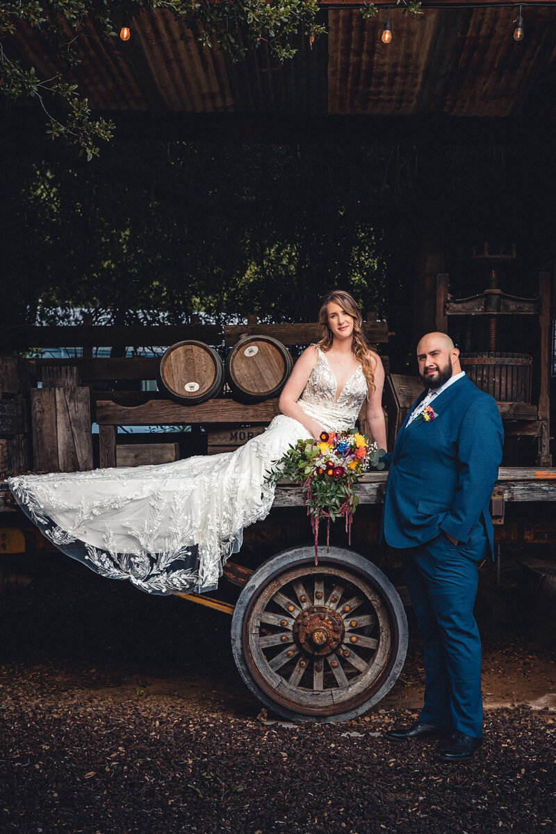Bride sitting on horse cart  with colorful florals and  groom standing next to her