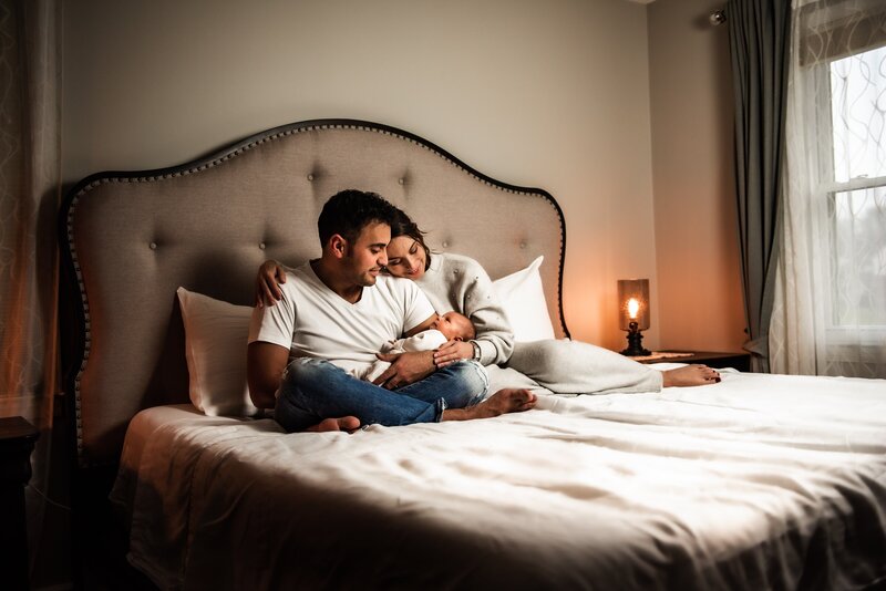 New parents in bed holding baby, J Holsey Photography