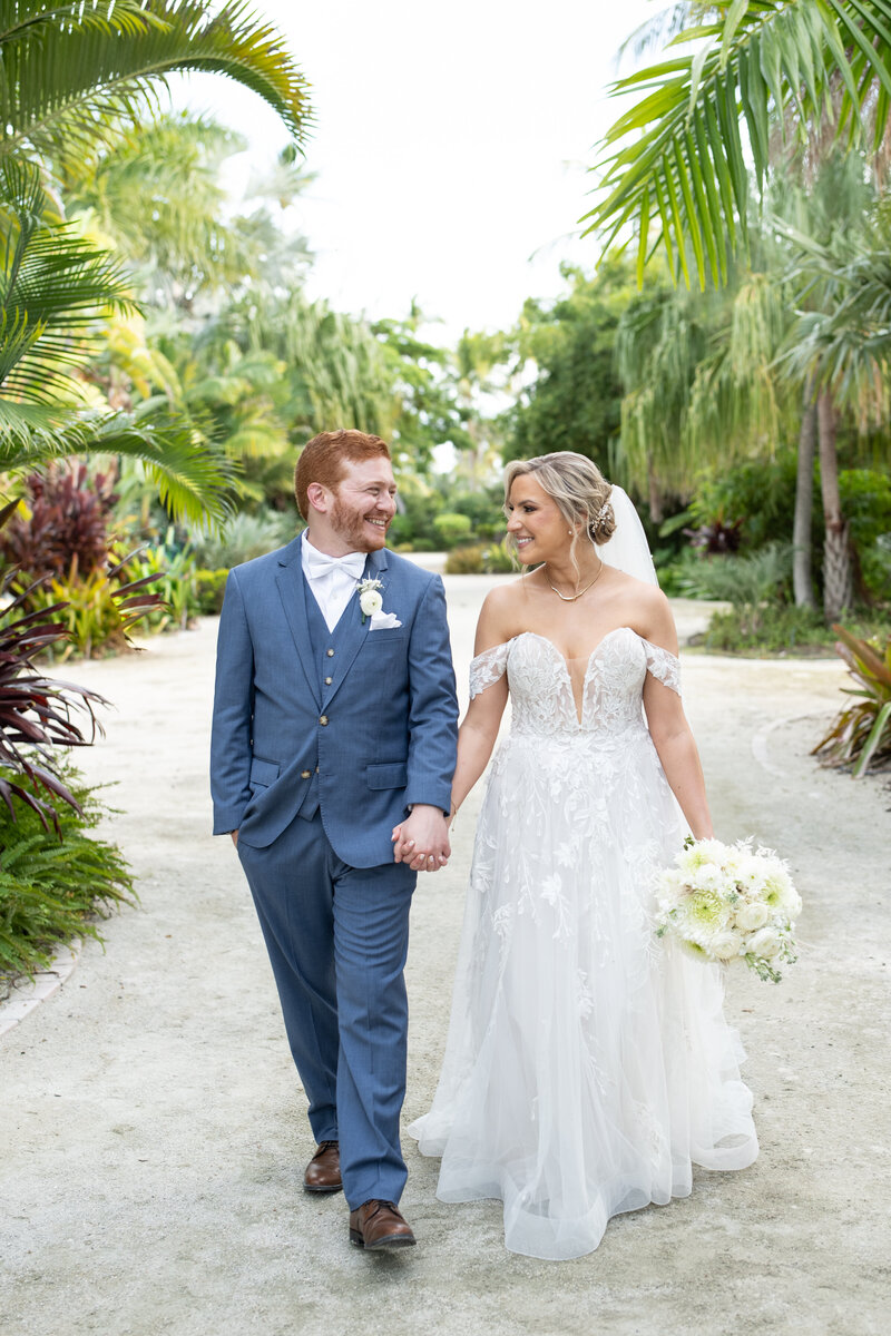 Bride and groom holding  hands  near palm trees in Naples Florida