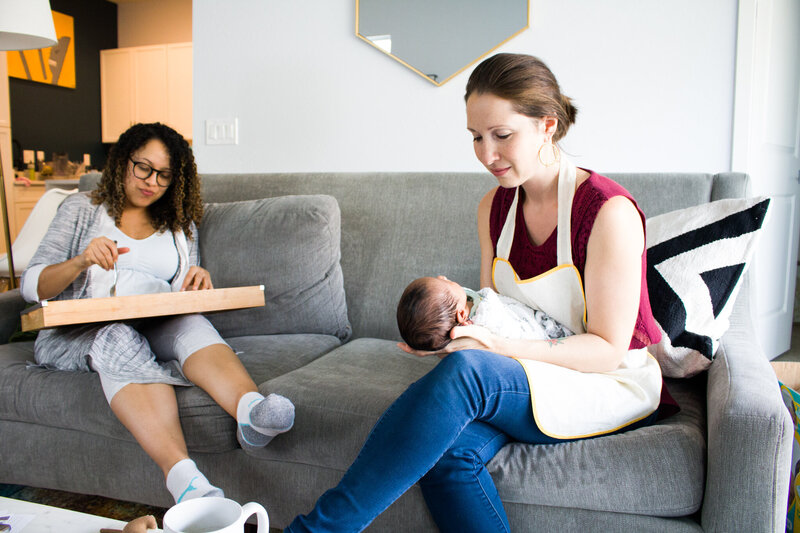 Woman in a red shirt sitting on a couch holding a baby next to another woman