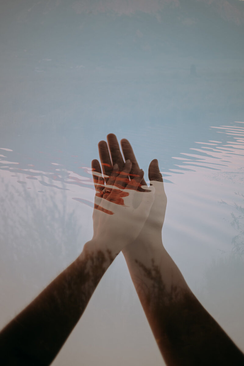 Two hands rest together, one with an engagement ring. Water is overlayed with half transparency