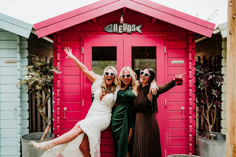 two brides in white outfits holding hands one bride holding her bouquet above her head with round stone door entrance in background fun aberdeen wedding photography