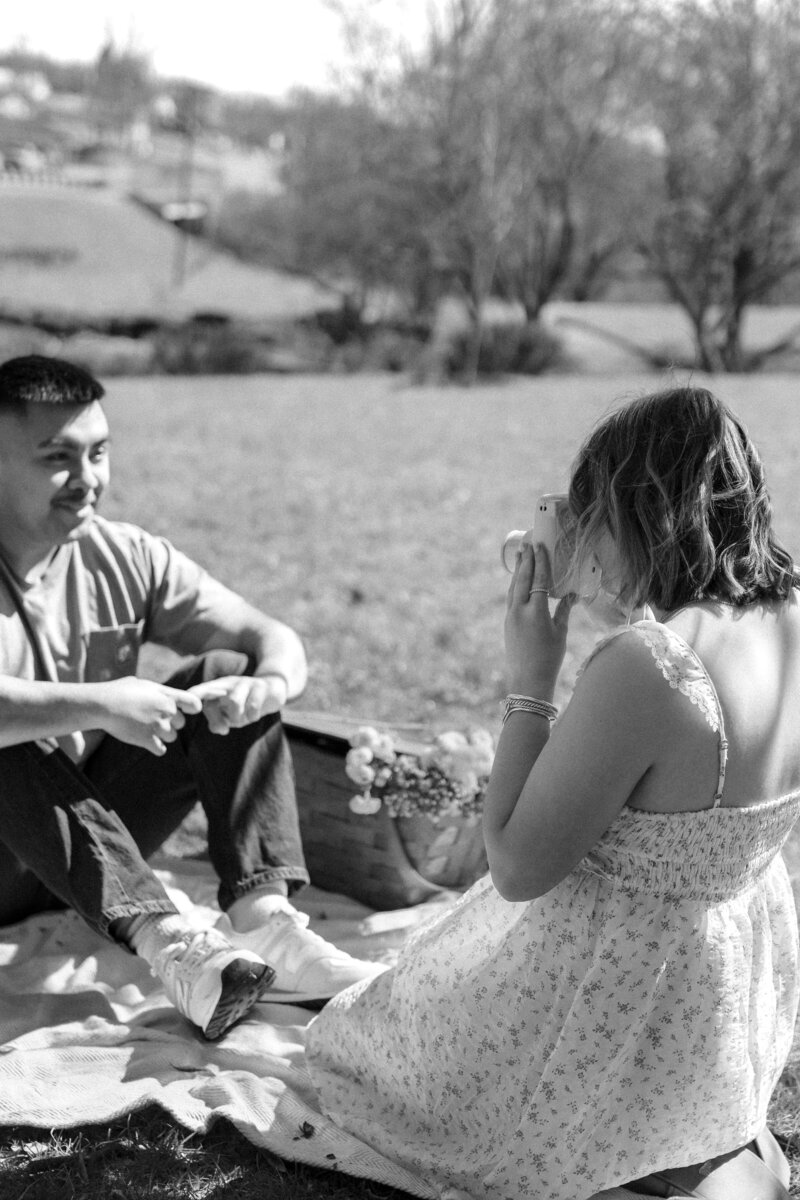 Engaged couple taking polaroids of each other during their outdoor engagement session at a scenic Kentucky park, captured by Abby Dutra Photography.