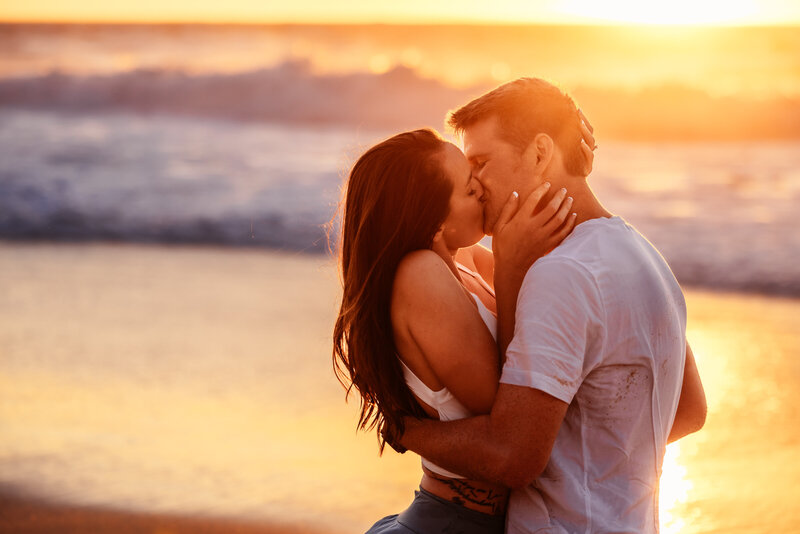 Shannon Lee, a Florida elopement photographer capturing an intimate kiss between a couple on the beach at sunset, with waves crashing in the background.