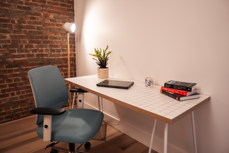 Furnished Brooklyn office for rent featuring brick walls, a large desk area, blue rolling office chair and more.