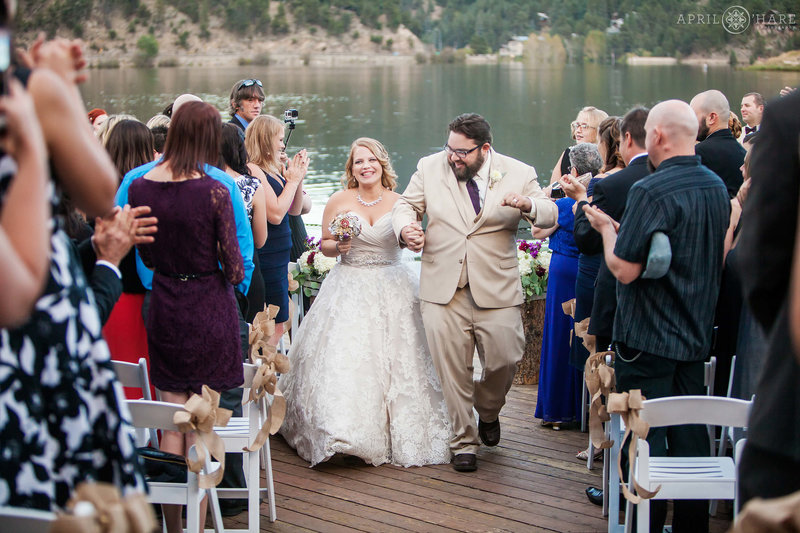 Happy bride and groom walk down the aisle together at the end of their ceremony on the back deck of the Evergreen Lake House in Colorado