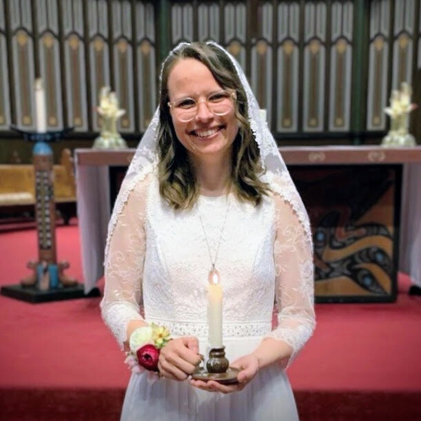 a young woman in a wedding dress holding a candle during a consecrated virginity ceremony