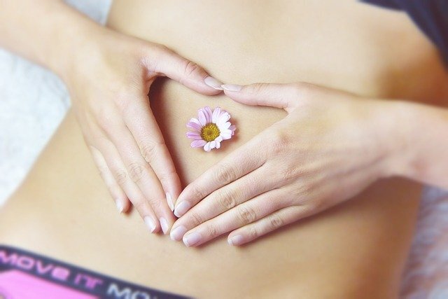 two hands resting in heart shape on stomach with flower in belly button