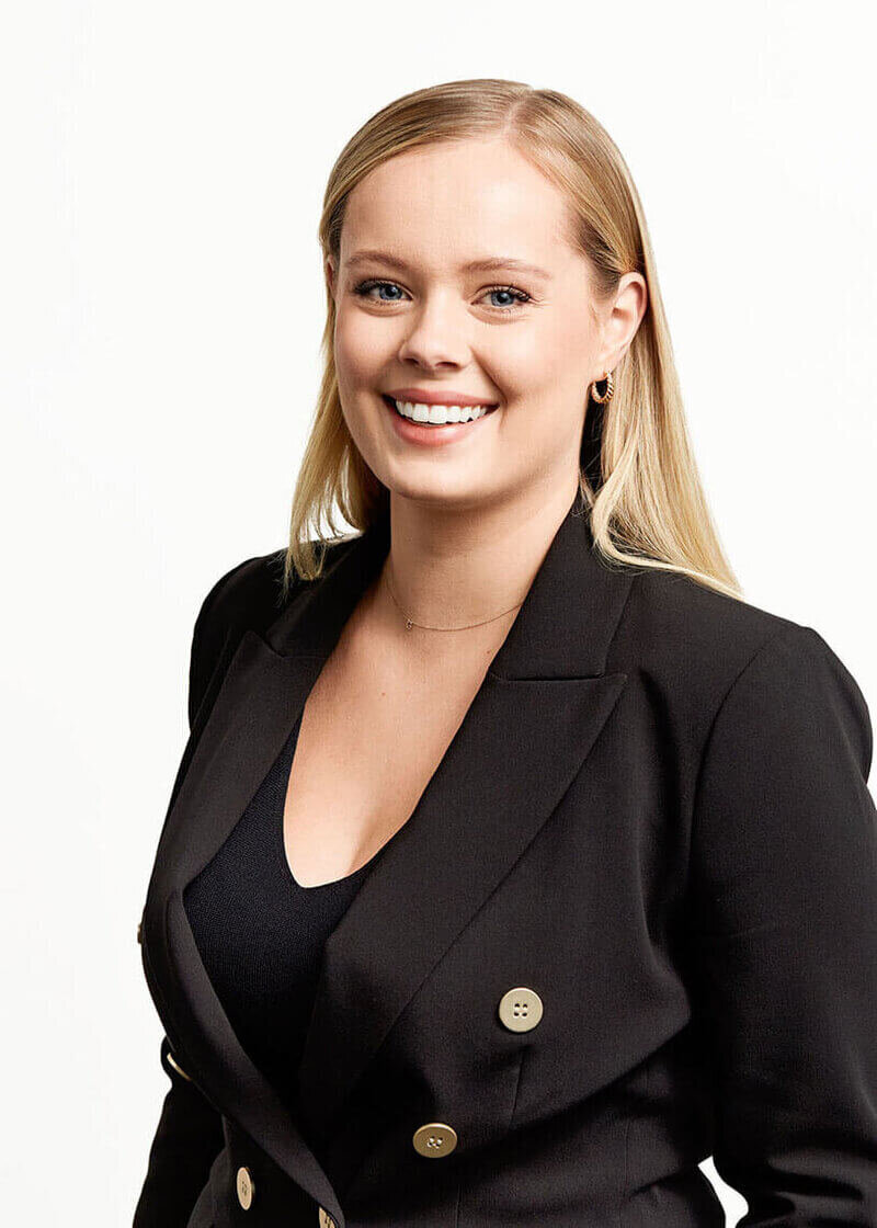 Blonde woman smiling with black blazer against white background.