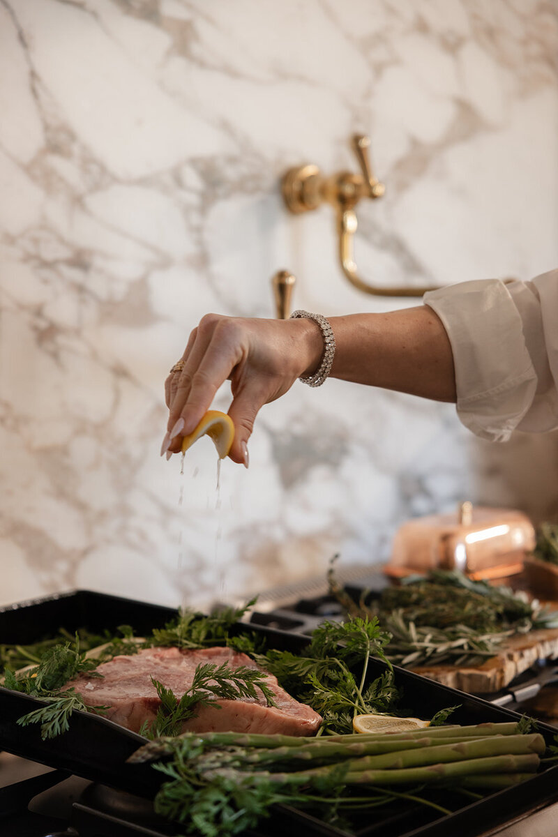 Functional dietician and nutritionist Tracy Greenstein squeezing lemon on a steak with herbs and asparagus for a nourishing, balanced meal