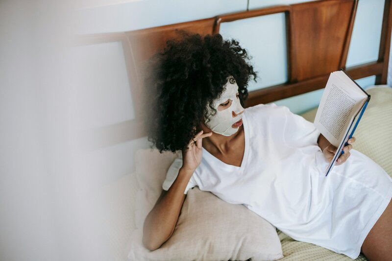 Woman reading on bed with a facemask