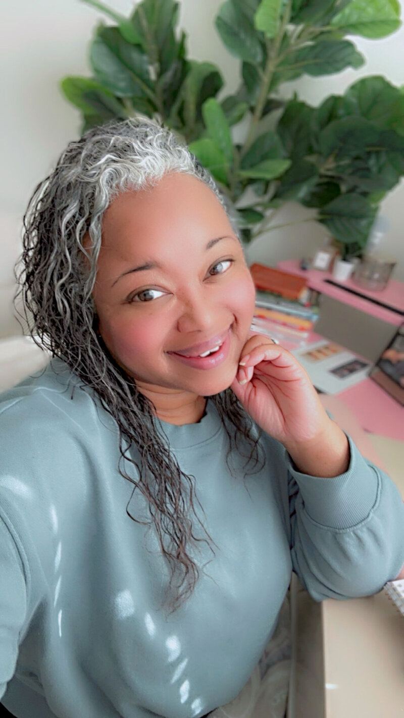 Letitia Hopkins, Founder of Encourage Over Everything, smiling confidently at her desk with her hand gracefully resting under her chin, embodying self-love, leadership, confidence, and Main Character Energy.
