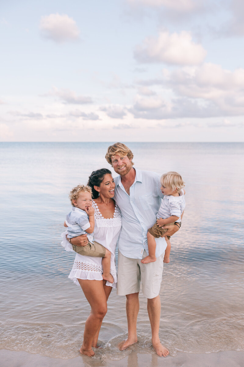 family of four standing in the ocean while smiling