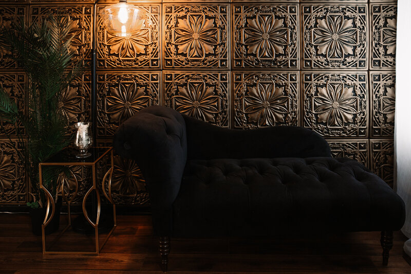 gold wall with black chaise lounge and lamp