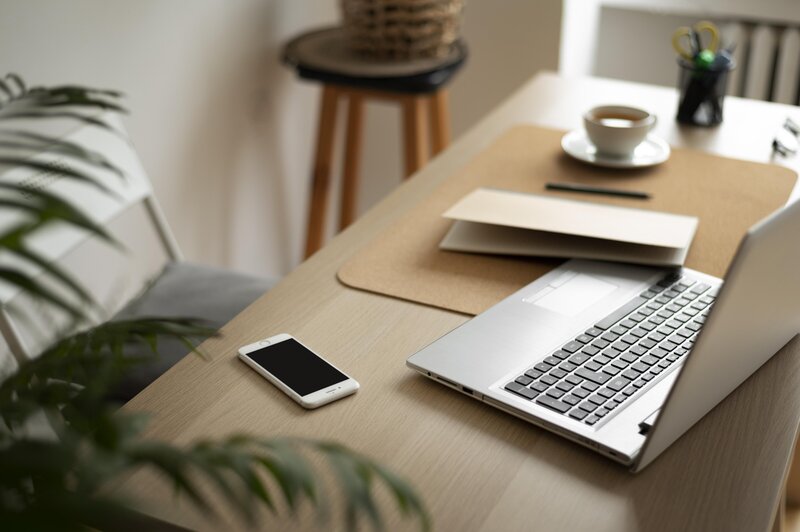 Laptop and phone on a desk with a plant in the foreground