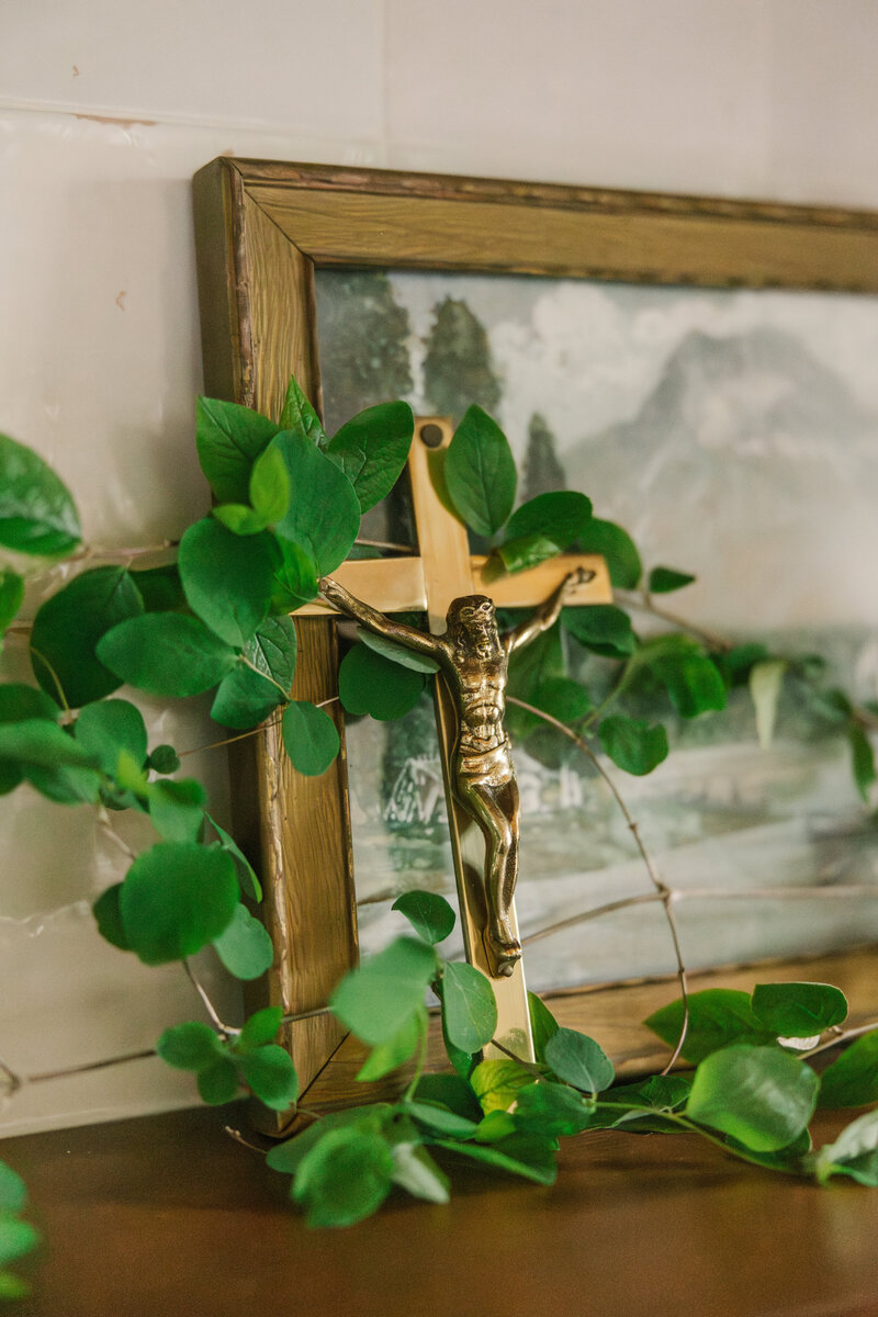 Gold crucifix leaning against framed artwork with greenery around it