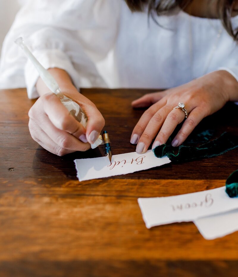 Close up of writing calligraphy place cards with deckled paper, velvet green ribbon, and gold ink