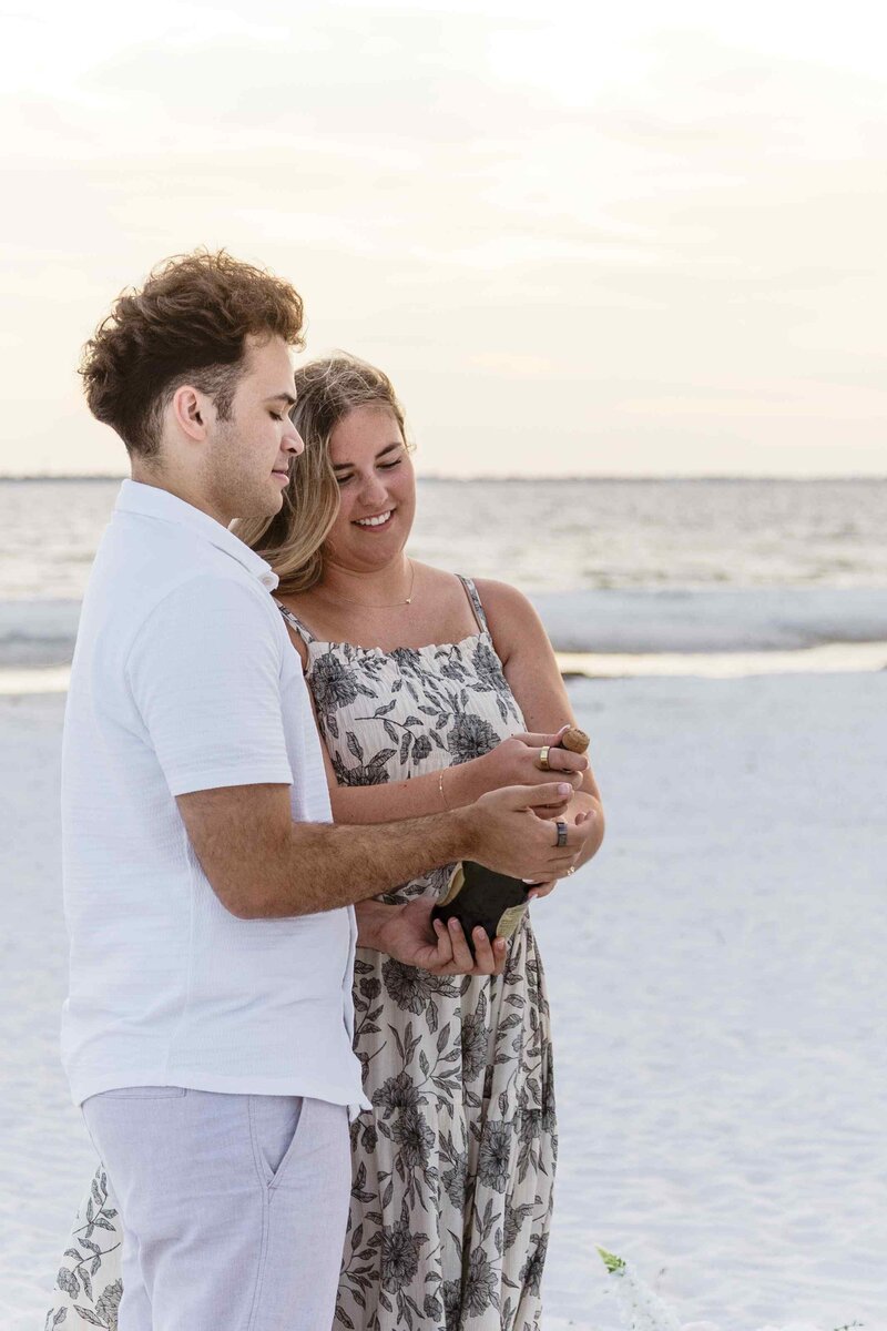 Couple opening champagne bottle together on the beach