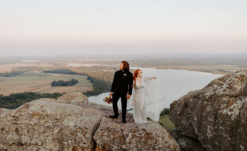 An eloping couple stands on a large boulder atop Petit Jean Mountain in Arkansas.