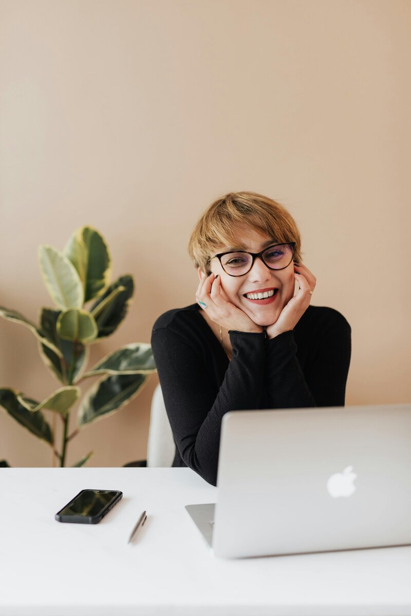 woman with glasses sitting at desk with laptop 