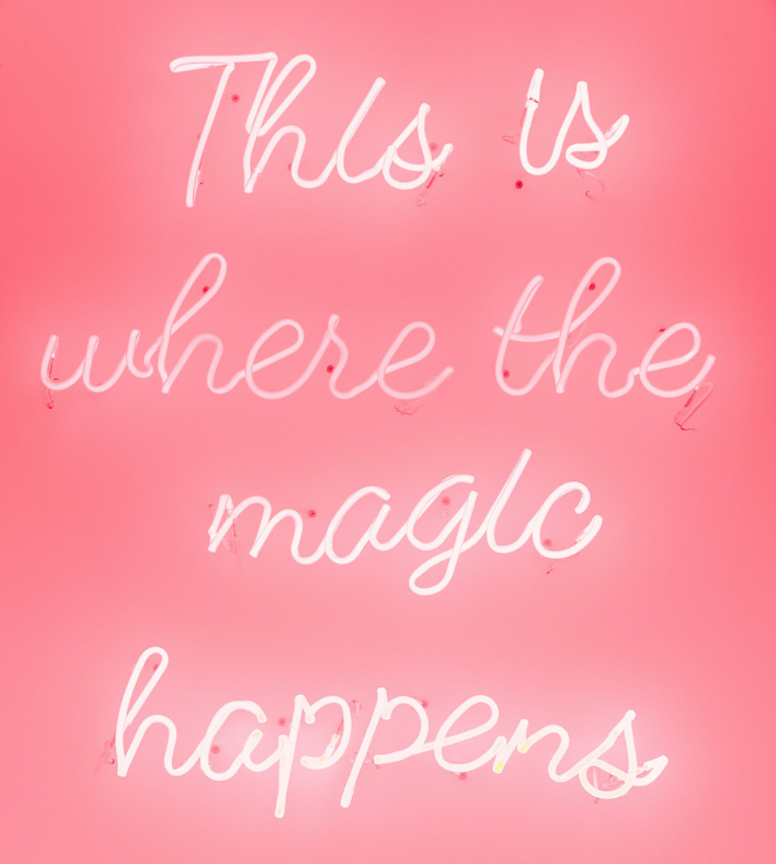 pink background with white neon letters that say "this is where the magic happens"