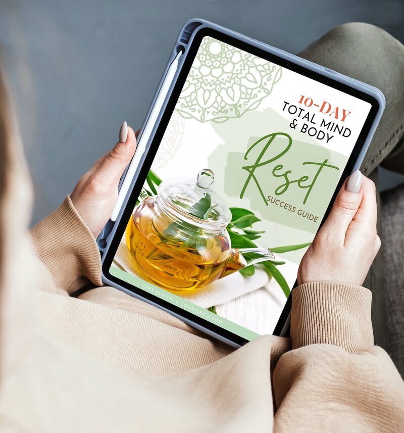 Hands holding a tablet displaying a '10-DAY TOTAL MIND & BODY Reset' guide with a teapot and cup in the background