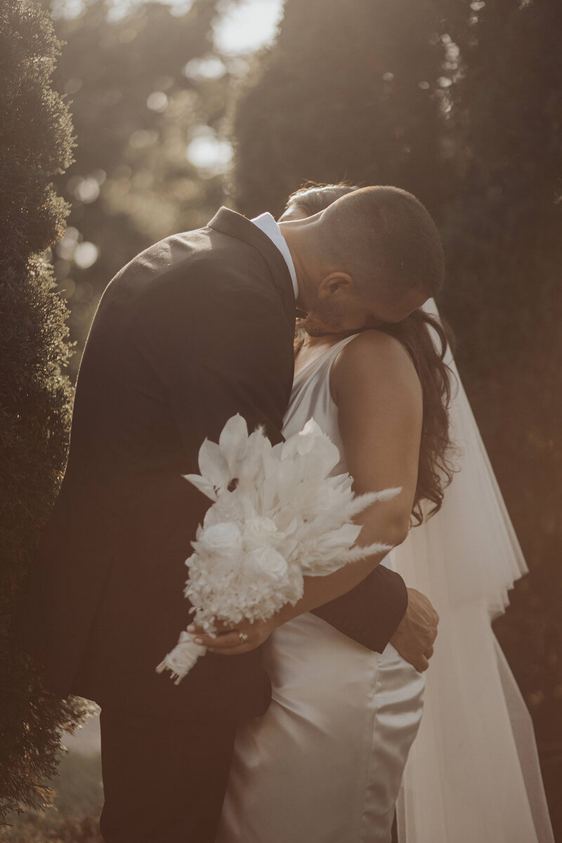 A sunlit embrace of a couple with a sharp-focus bouquet.