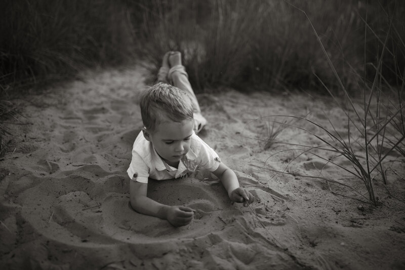Black and white image of Stephen and Kaity’s son playing in the sand dunes, captured in a nostalgic, documentary-style moment by Rainstorm Photo & Video.