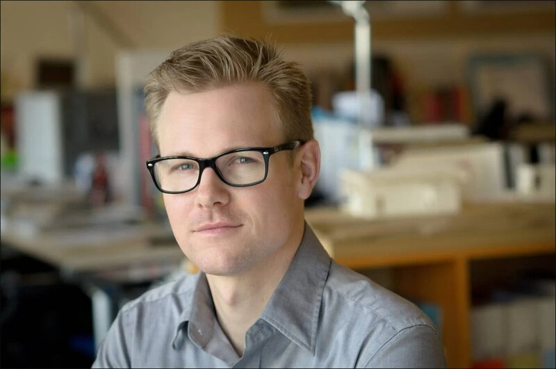 ALT: NYC professional headshot of young businessman with glasses in modern office setting