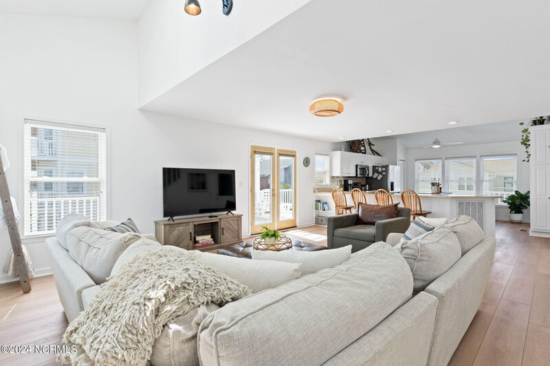 Open floor plan kitchen and living room with high ceilings, stainless steel appliances, wooden island, and visible second level in spacious home.
